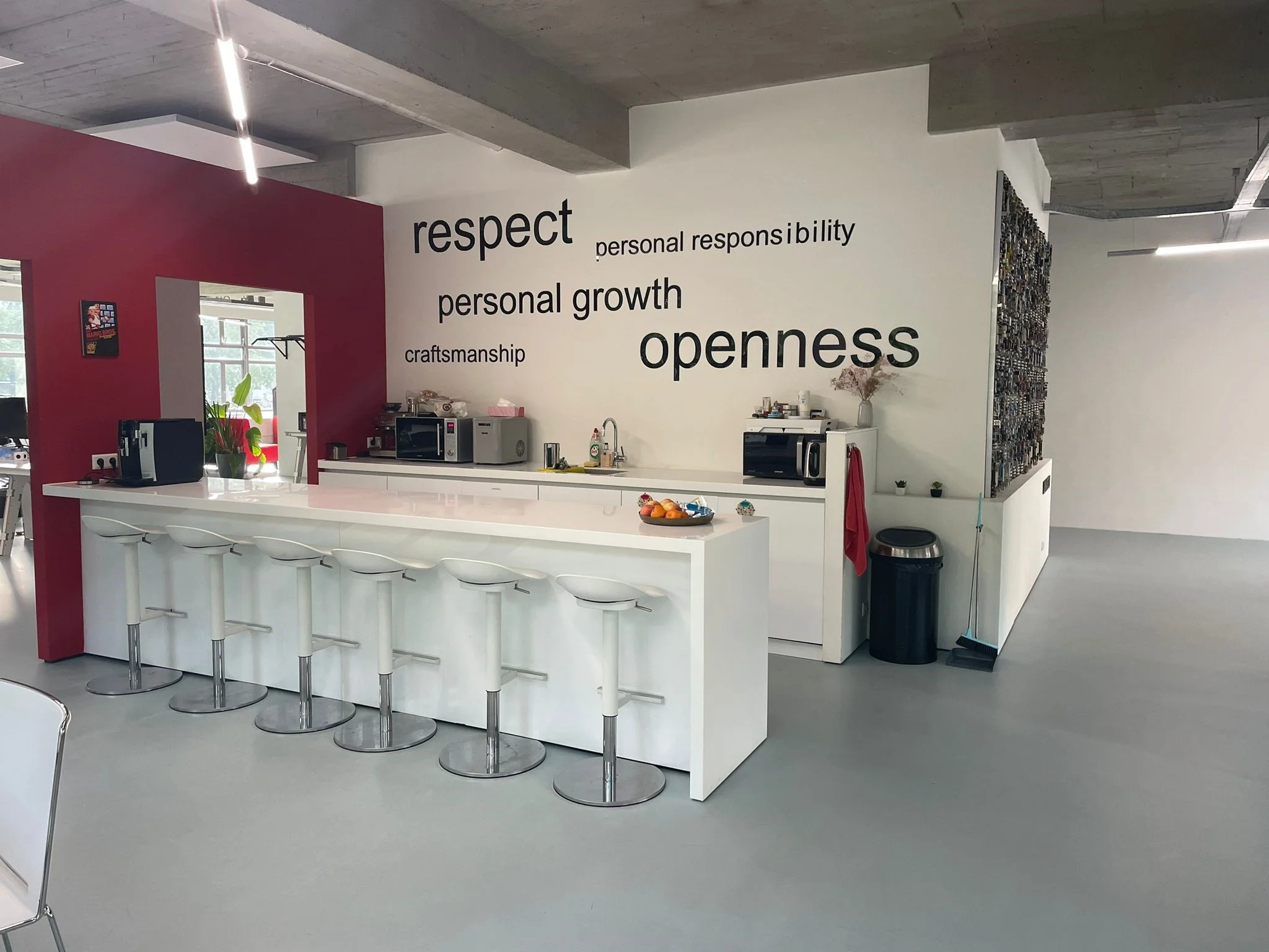 Moderne kantoorkeuken met een witte bar, barkrukken en inspirerende kernwaarden op de muur aan de Van Leijenberghlaan.